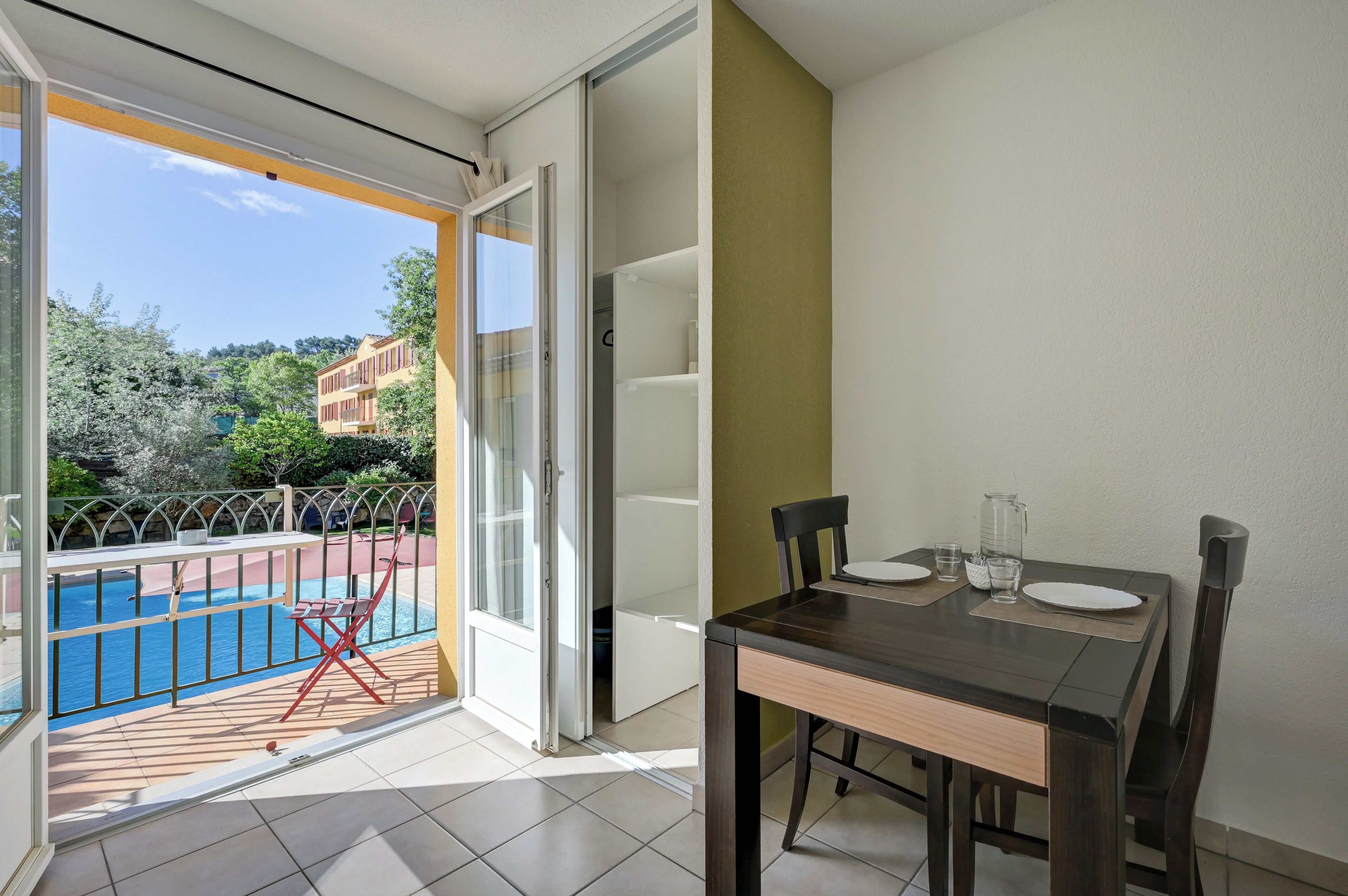 Un balcón con piscina, una mesa de comedor con sillas y una puerta corrediza de cristal.