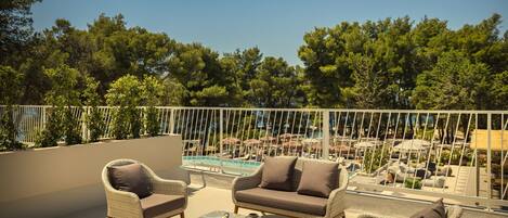 A balcony with wicker furniture, a pool, and a view of trees.
