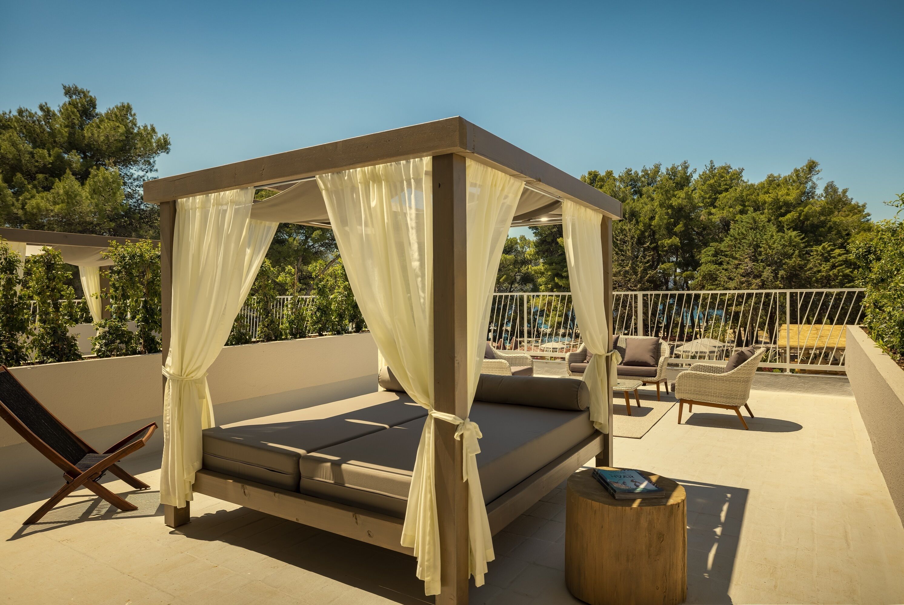 Un balcon privé donnant sur l’extérieur, doté d’un lit à baldaquin, de chaises longues et d’une table en bois.
