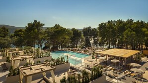 A rooftop pool area with lounge chairs and umbrellas, surrounded by trees and overlooking a body of water.