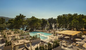 A rooftop pool area with lounge chairs and umbrellas, surrounded by trees and overlooking a body of water.