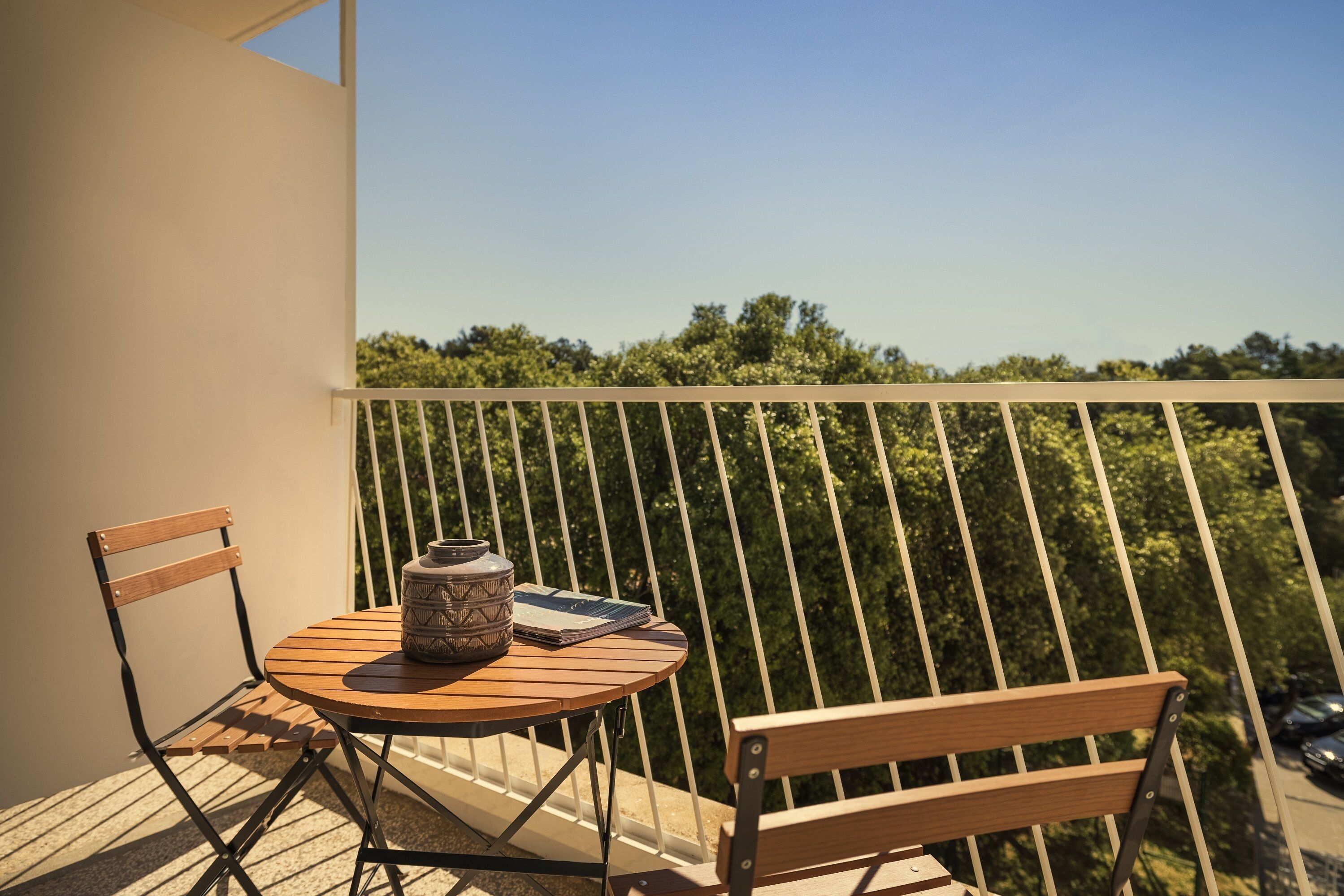 Een balkon met een ronde houten tafel en twee houten stoelen, een decoratieve vaas en een notitieboekje.