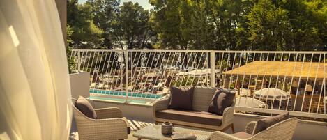 Un balcon agrémenté de meubles en osier, d’une table en verre et offrant une vue sur une piscine et des arbres.