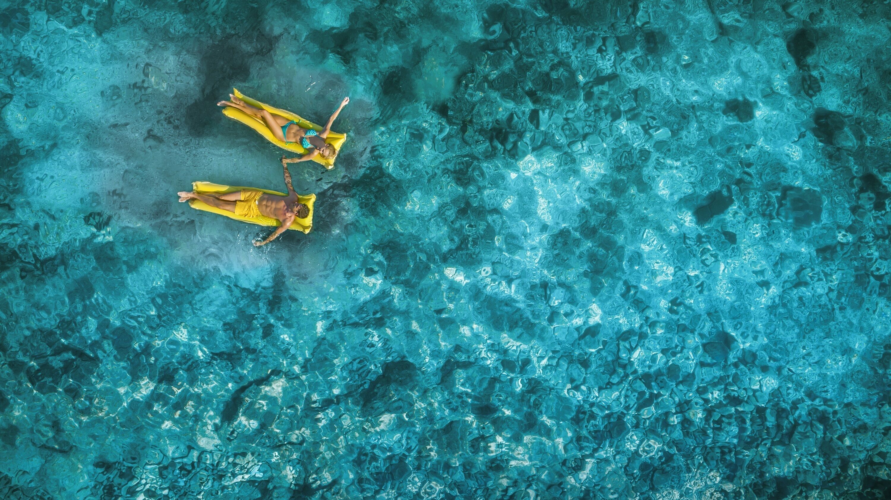 An aerial view of a swimming pool with clear blue water and two yellow floating platforms.