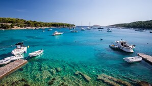 Ein Hafen mit mehreren Schiffen, klarem türkisblauem Wasser und einer felsigen Küstenlinie mit Bäumen.