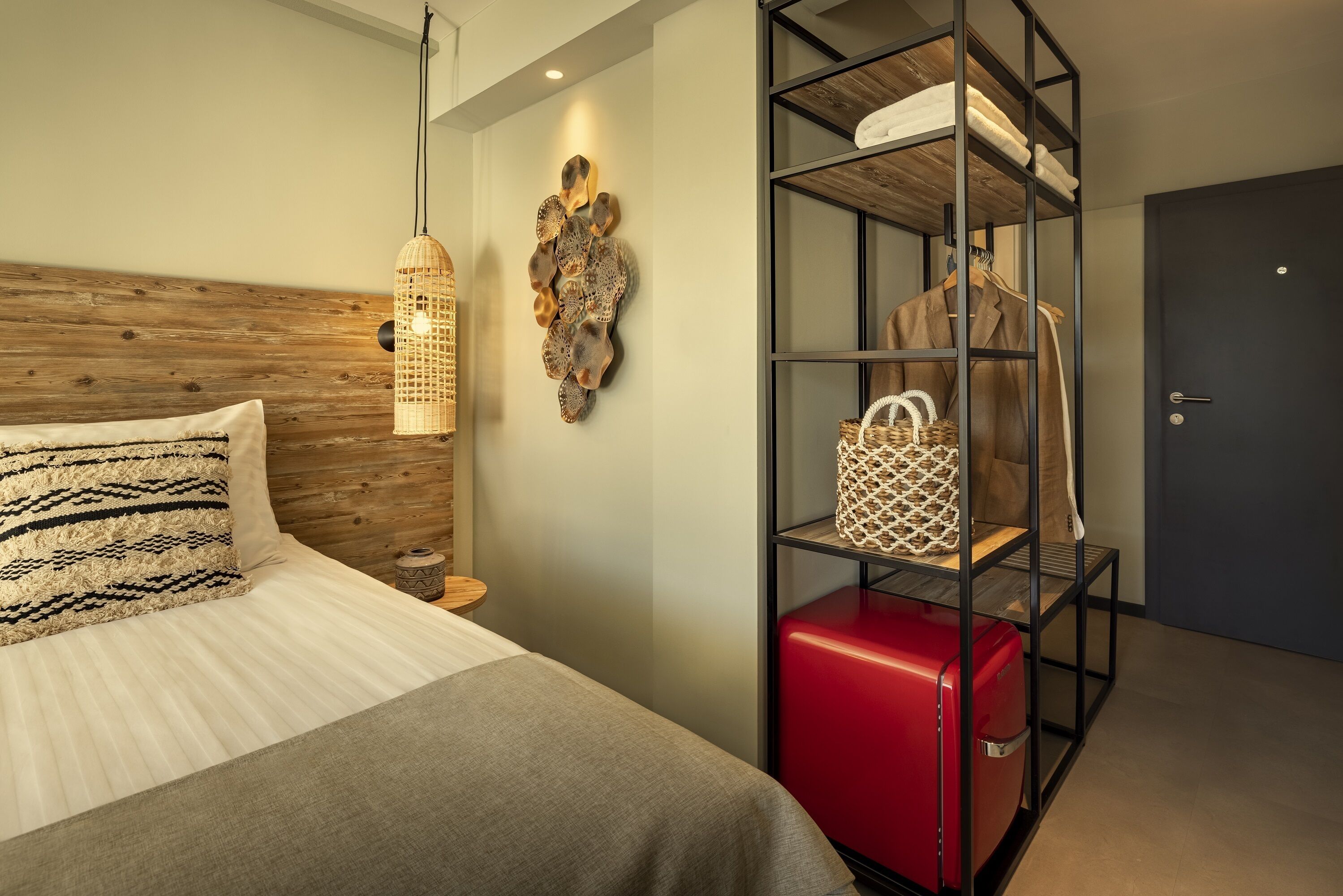 Habitación de hotel impecable con una cama, una maleta roja, un armario y un adorno en la pared.