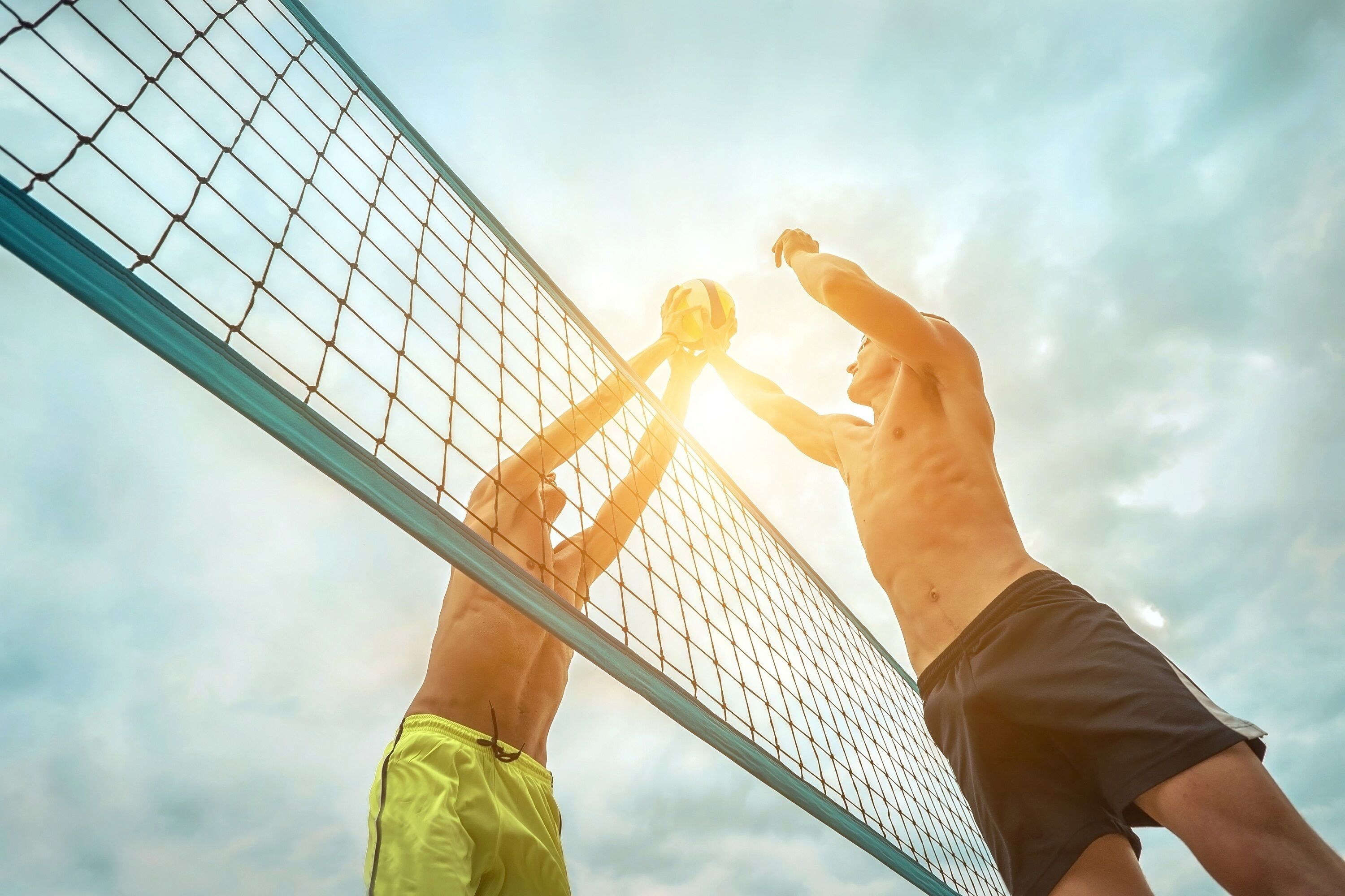 Zwei Personen spielen Beachvolleyball in der Nähe eines Netzes.