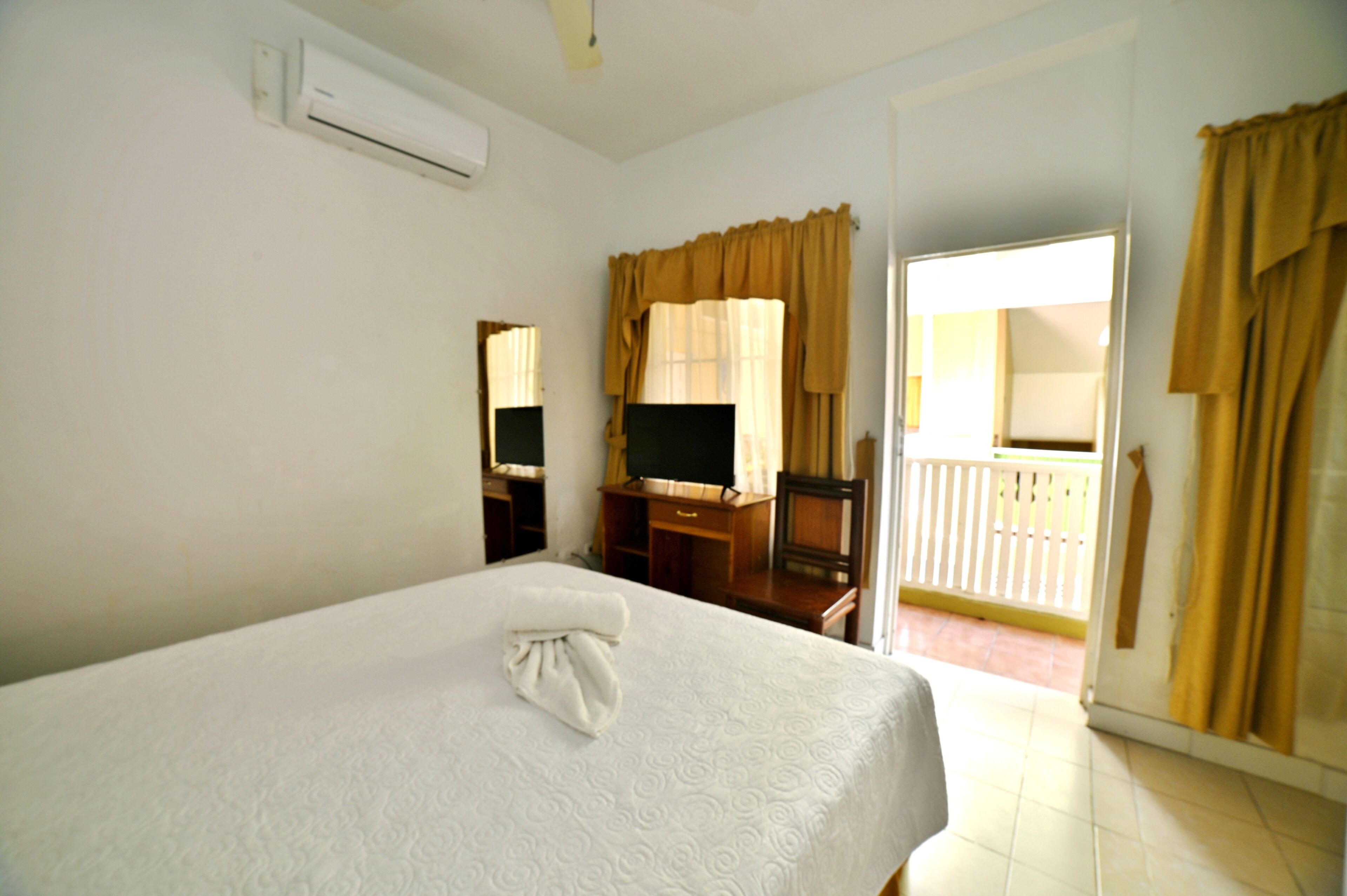 A hotel room with a bed, a desk, a chair, a television, and a balcony.