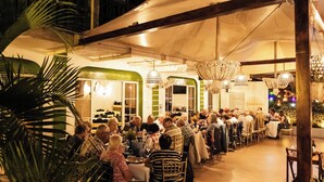An outdoor dining area with tables and chairs, surrounded by potted plants and a large tent structure. - Hotel Petén (Flores)