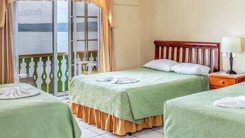 Habitación de hotel con dos camas, cabecera de madera, mesita de noche con lámpara y vista a un cuerpo de agua a través de una puerta corrediza.