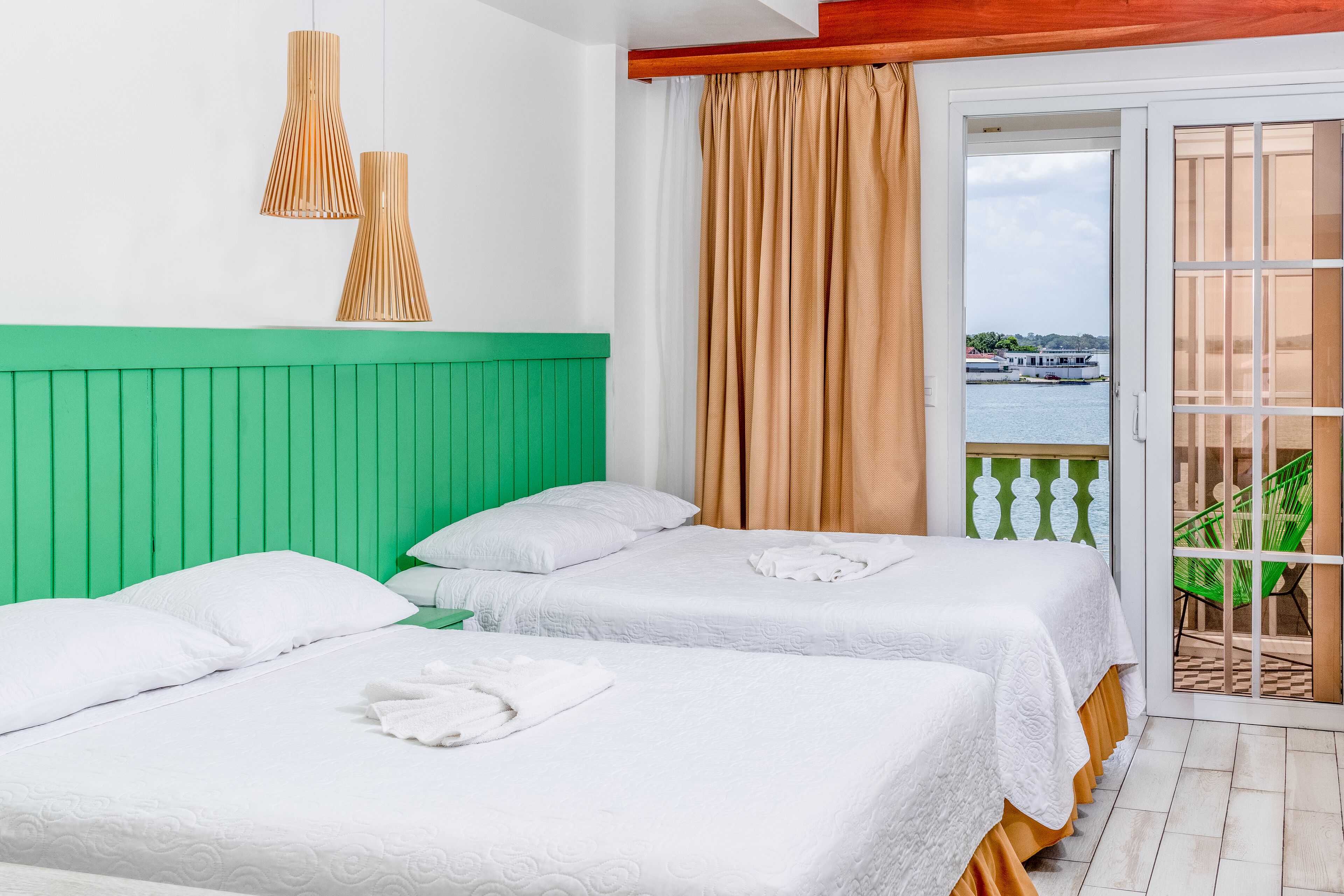 A hotel room with two beds, a green headboard, white bedding, and a view of a body of water through a sliding door.