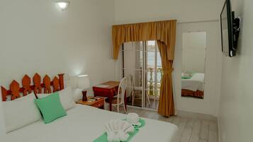 A hotel room with a bed, a desk, a chair, a window with curtains, a view of the sea, and a mounted TV.