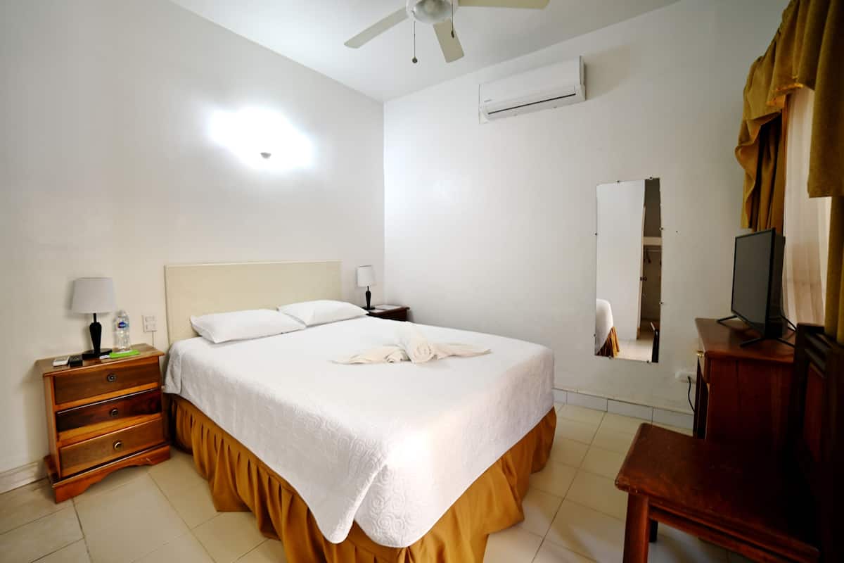 Una habitación de hotel con cama, mesita de noche, cómoda, televisor y aire acondicionado.