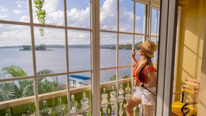 A room with a large window overlooking a body of water, a balcony with a green railing, and a wooden bench. - Hotel Petén (Flores)