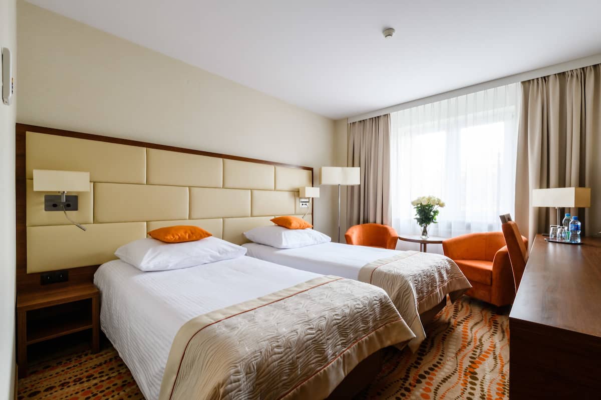 Habitación de hotel con dos camas, un escritorio, una silla y una pequeña mesa con un florero.