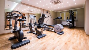 Un gimnasio con diferentes máquinas de ejercicio, un espejo grande y suelo de madera.
