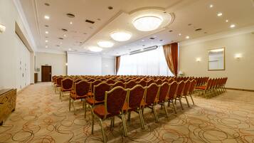A conference room with rows of chairs, a projector screen, and a large window with curtains.
