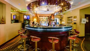 Zona de bar con barra circular, varios taburetes y una variedad de botellas y vasos en estantes.