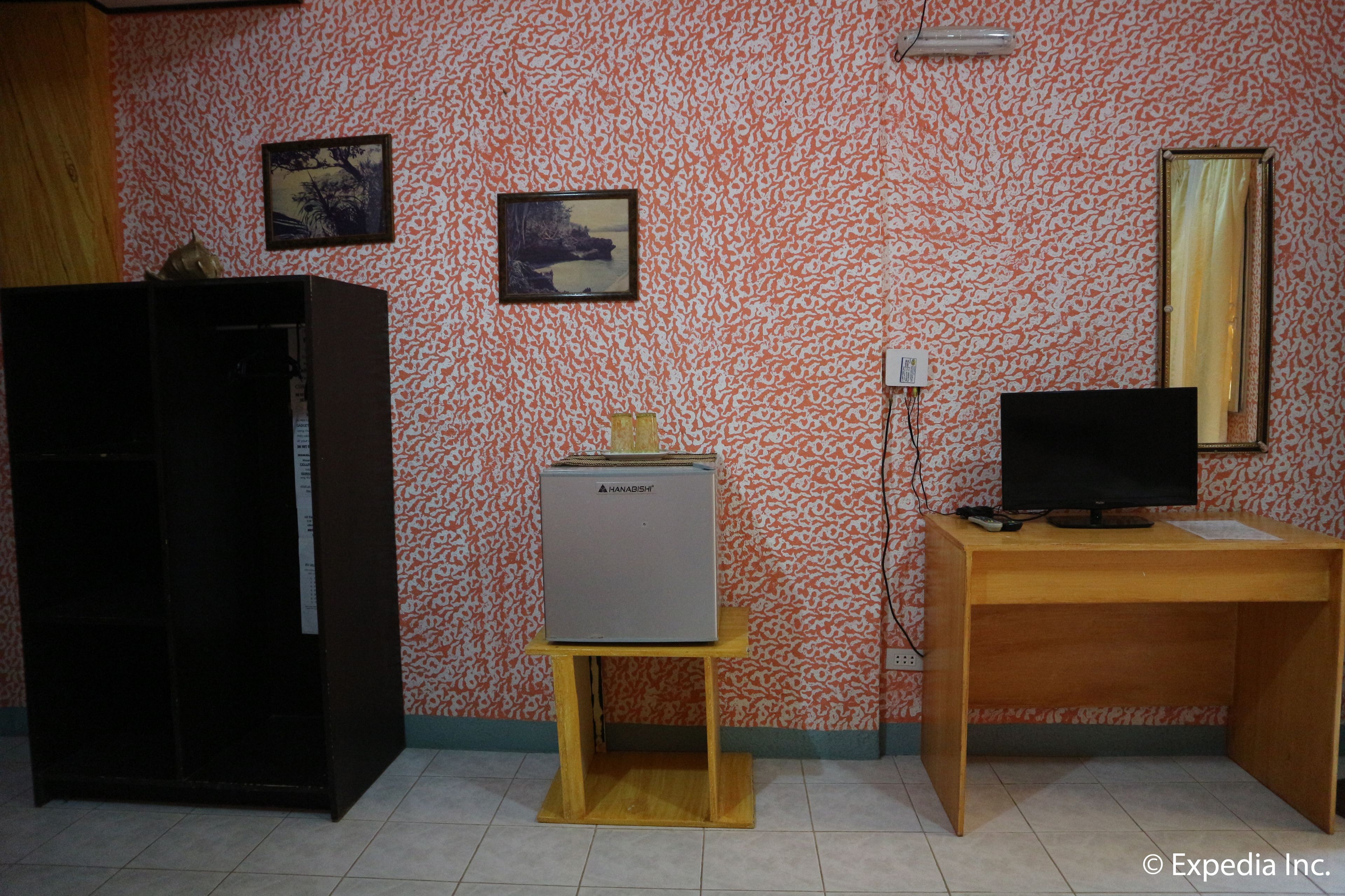 A room with a wooden desk, a computer monitor, a small cabinet, and two framed pictures on the wall.