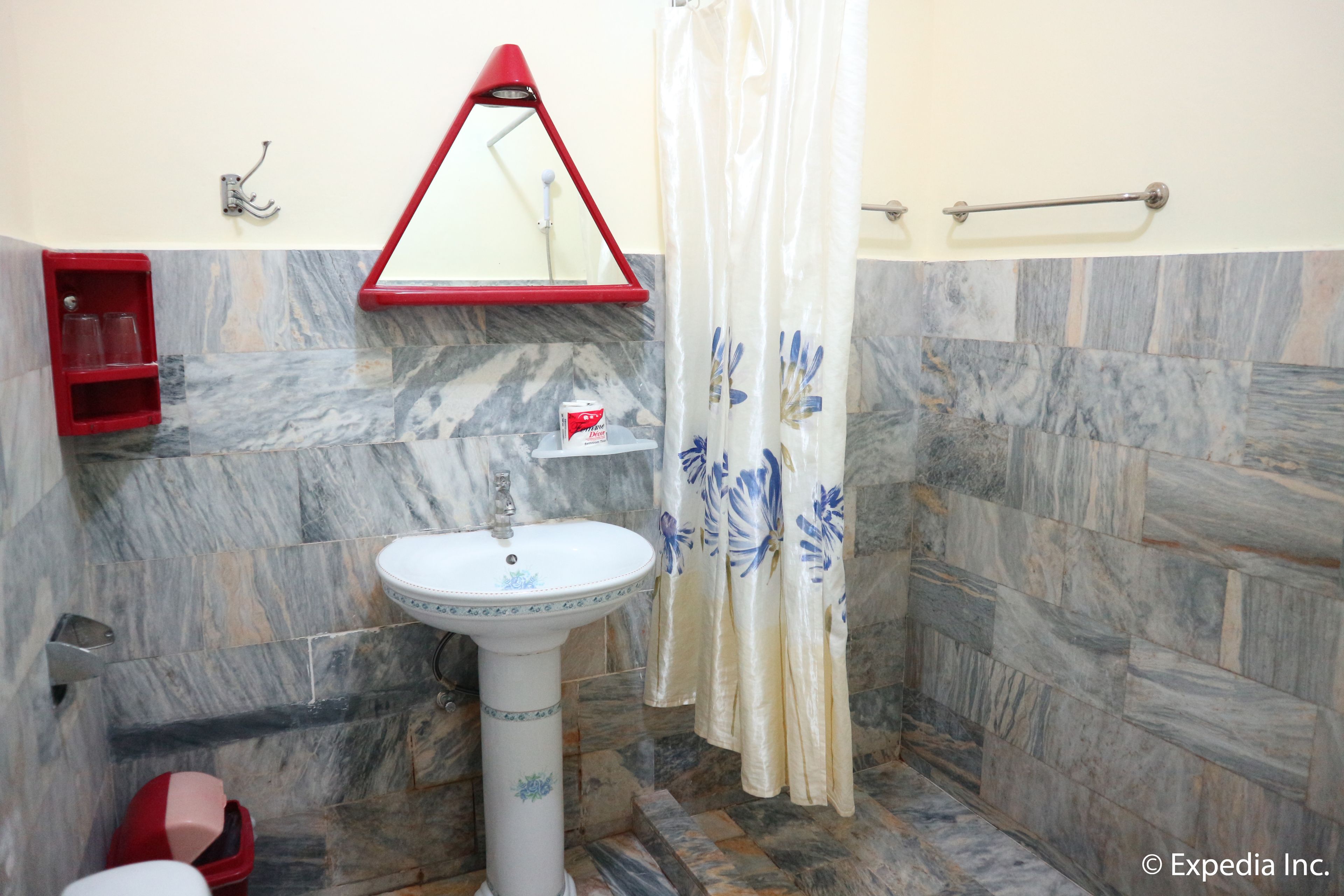 A bathroom with a pedestal sink, a red shelf with glasses, a red and white towel rack, and a shower curtain with a floral pattern.