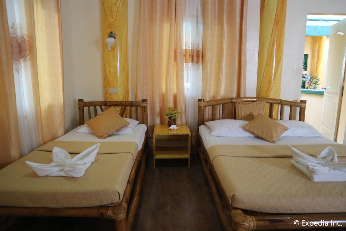 Une chambre d’hôtel avec deux lits en bois, une literie de couleur beige et une petite table de chevet en bois ornée d’un motif ananas.