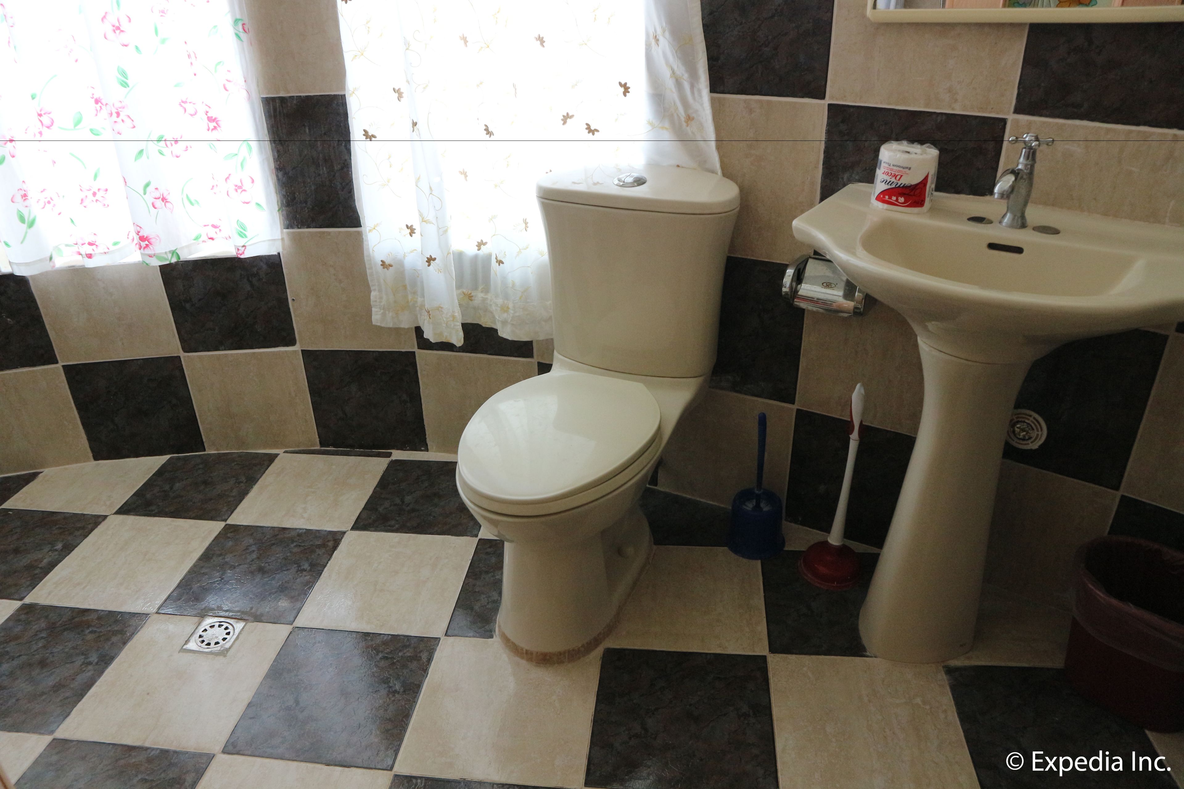 A bathroom with a toilet, sink, and a window with floral curtains.