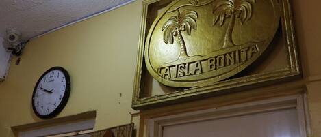 Een wandklok, een bord met palmbomen en de tekst 'TASLA BONITA', en een bordje met 'OFFICE'.