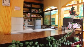 Un área de recepción con un reloj, un cartel que indica 'RESORT GUEST' lounge y lobby, una zona de cocina y un ventanal con vista a un edificio.