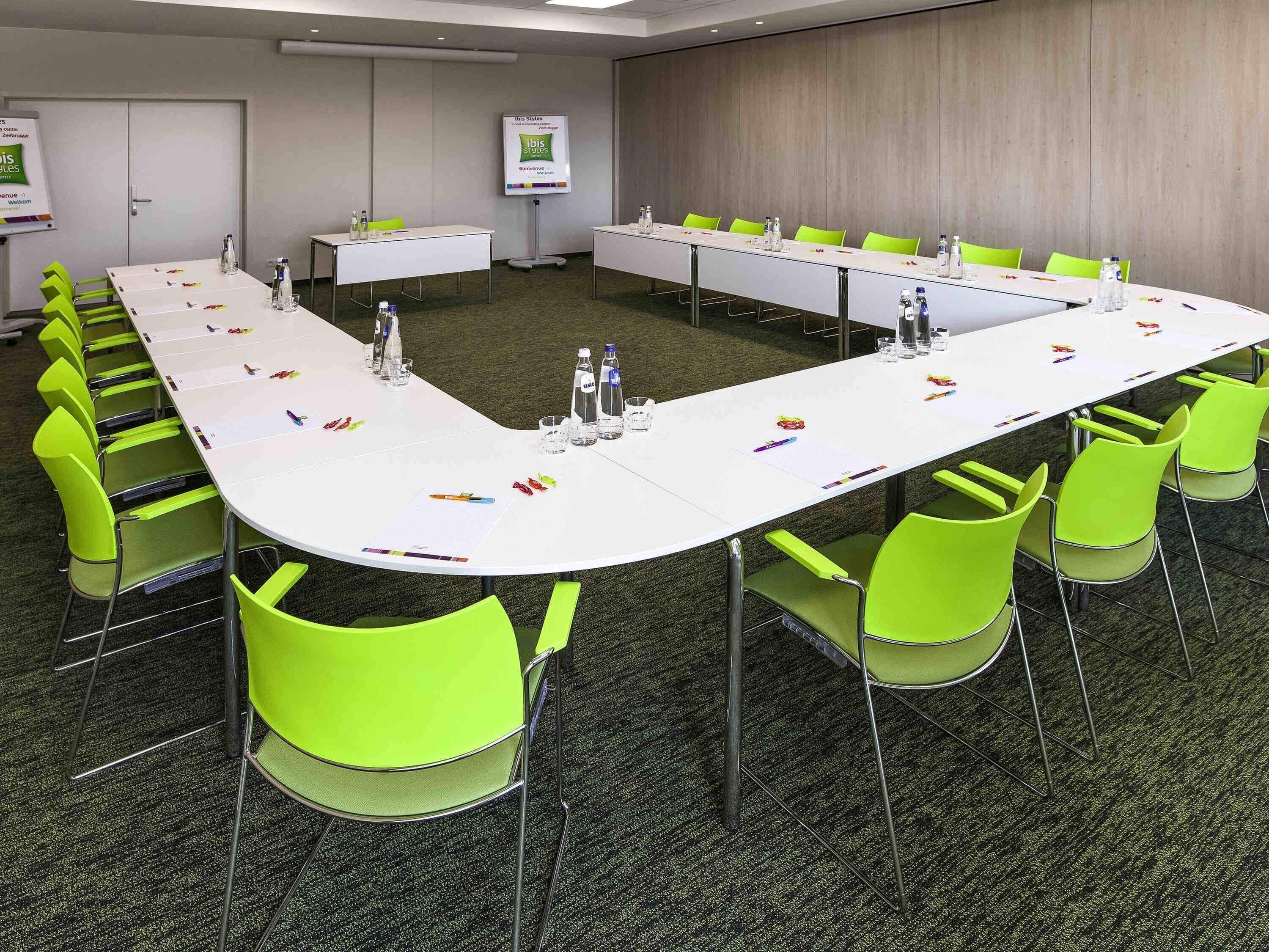A conference room with a long table, green chairs, water bottles, and a whiteboard.