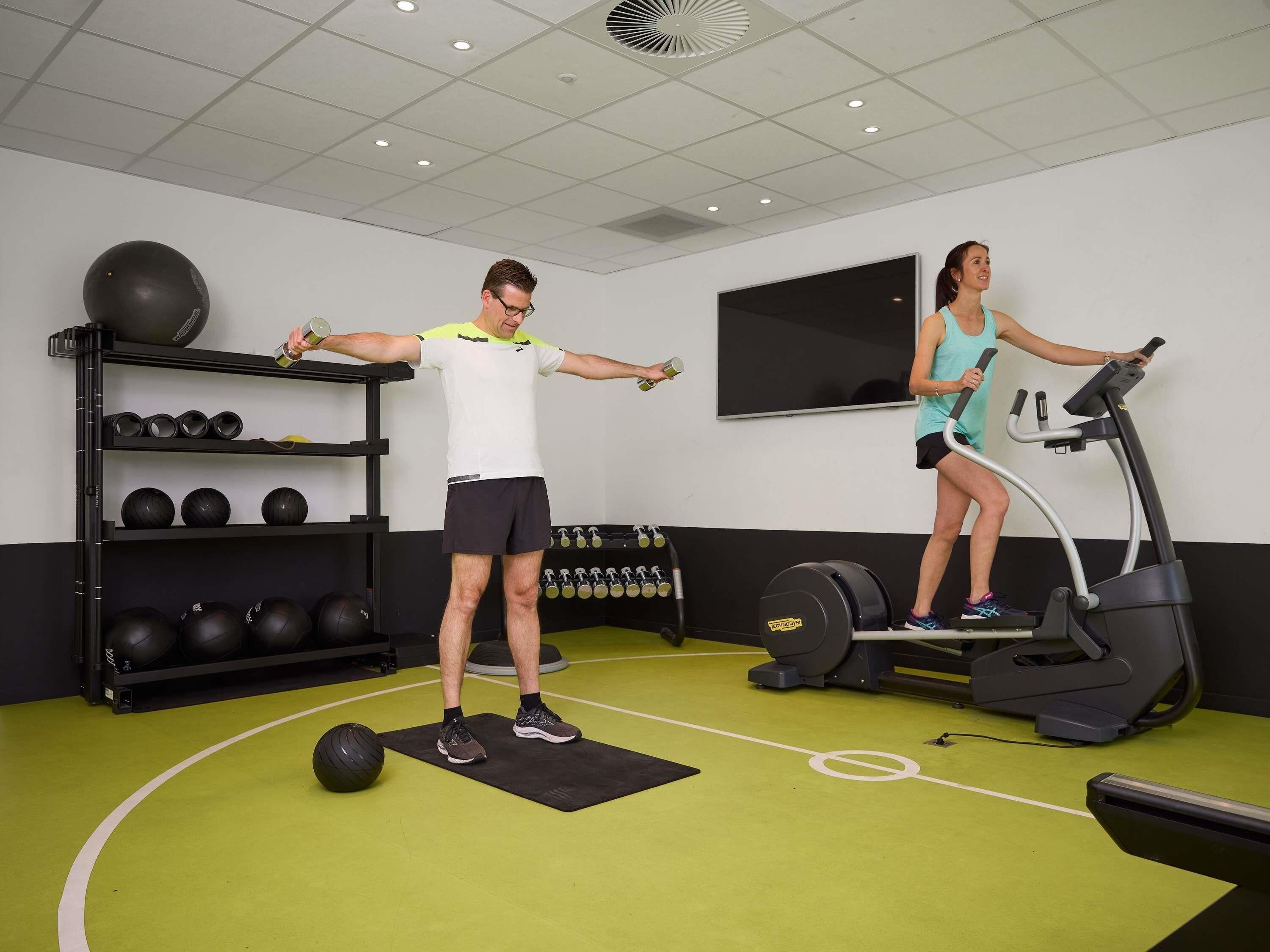 A gym with exercise equipment, a wall-mounted TV, and a shelf with exercise balls.
