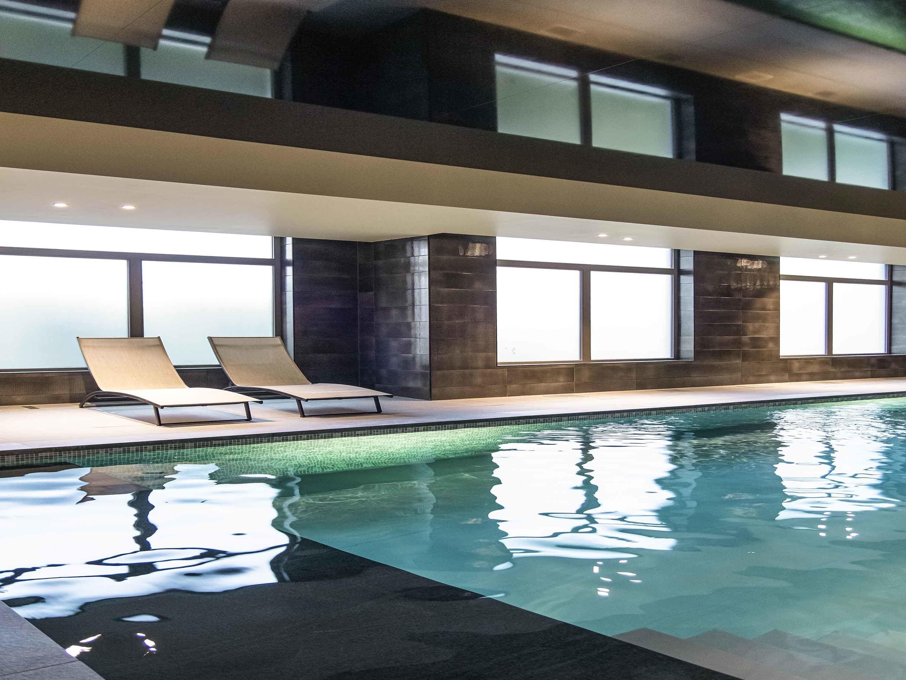 An indoor swimming pool with lounge chairs and large windows.