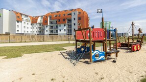 A playground with a swing set and climbing structures, adjacent to a building with orange roofs and multiple balconies. - ibis Styles Zeebrugge (Bruges)