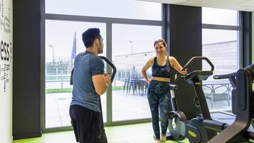 A gym with exercise equipment, large windows, and a view of the outside.