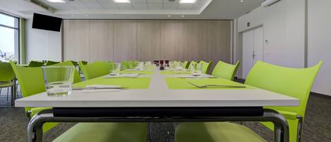 A conference room with a long table, green chairs, and a white tablecloth.
