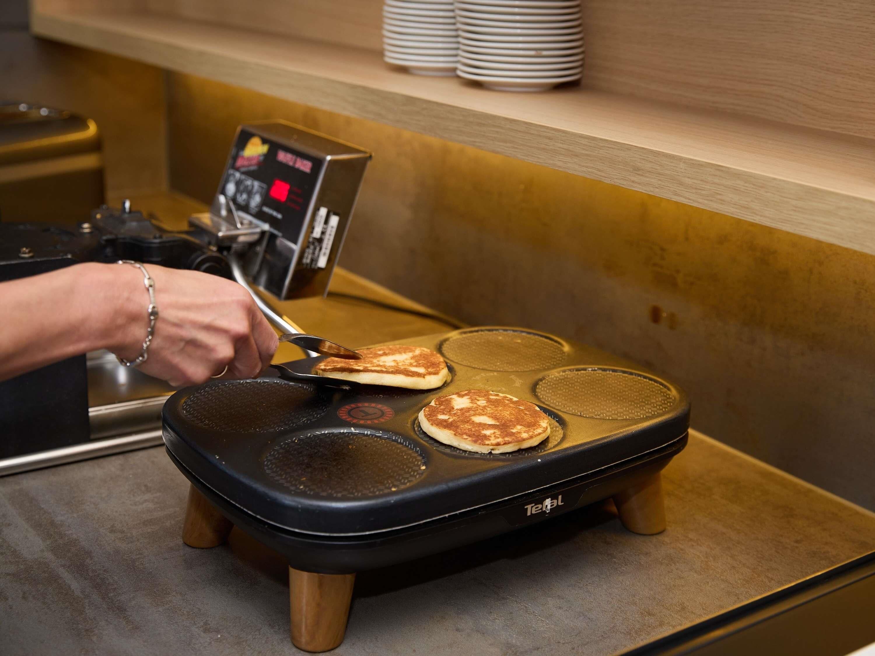 A waffle maker with a digital control panel and a person flipping a pancake.