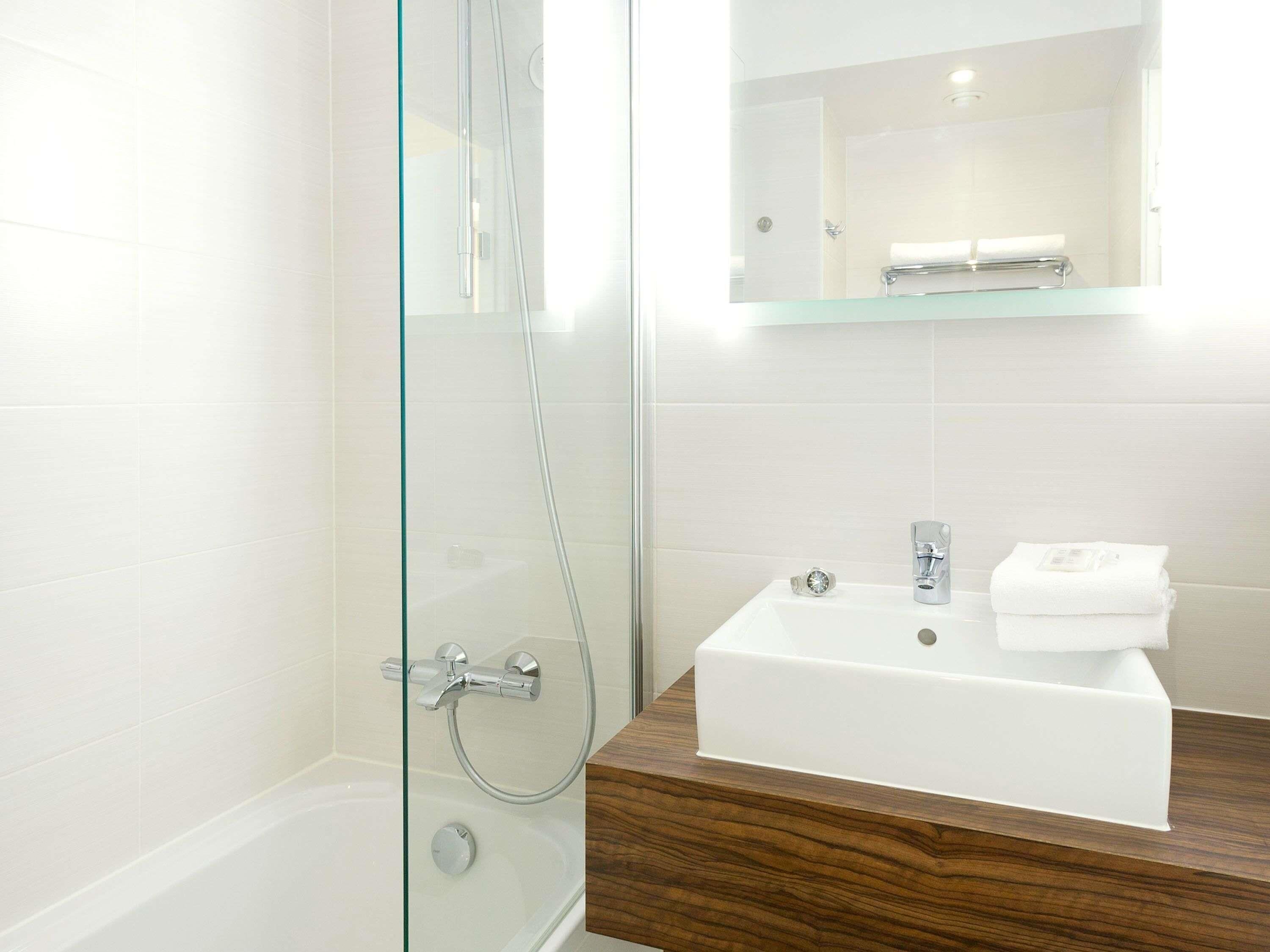 Une salle de bain moderne avec une douche à l’italienne en verre, un lavabo blanc doté d’un plan de travail en bois et un miroir au-dessus du lavabo.