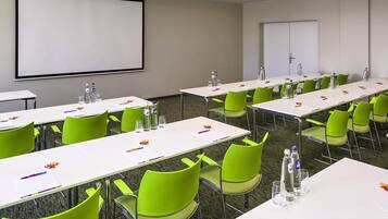 A conference room with white tables, green chairs, and a projector screen.