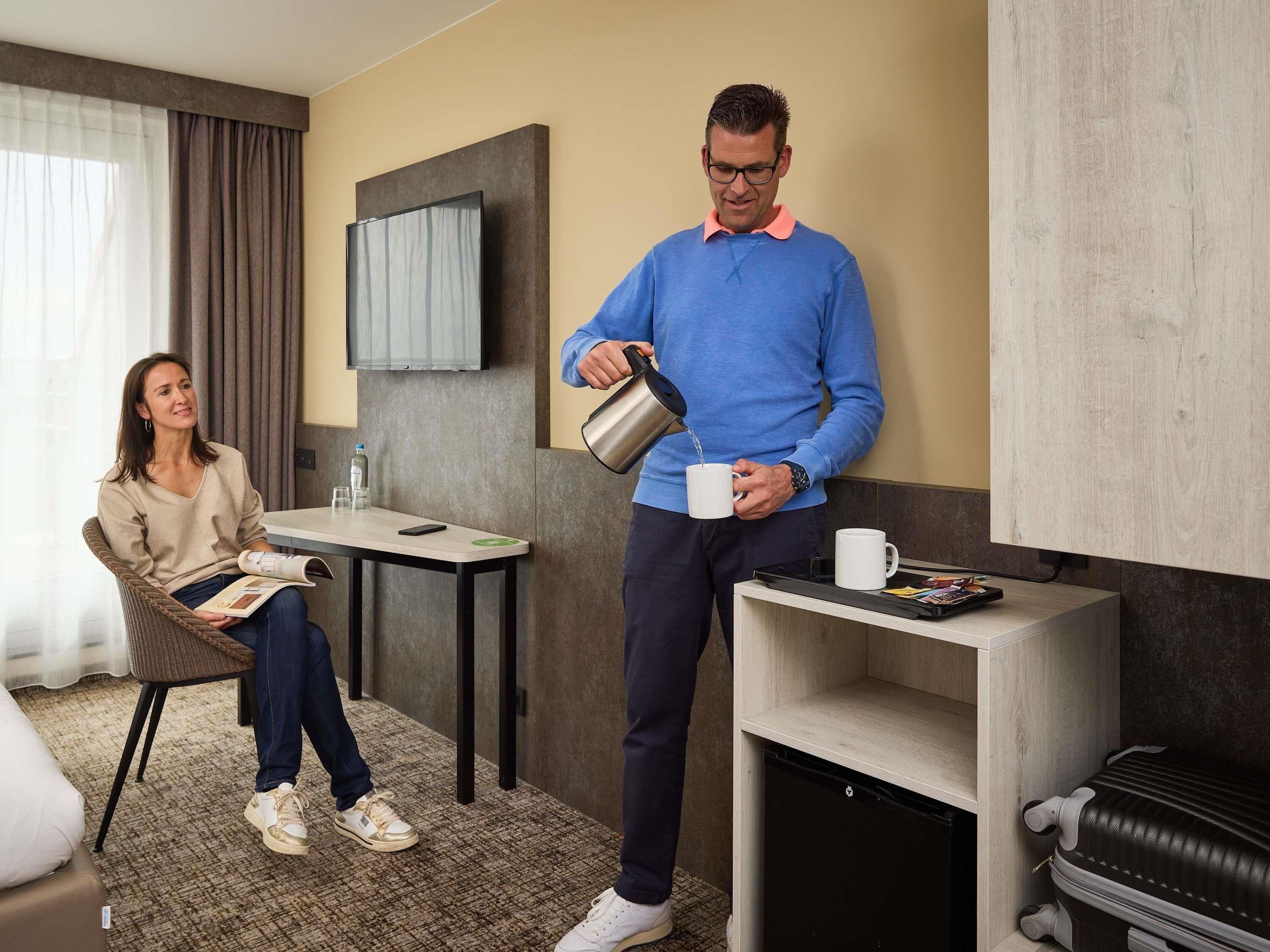A hotel room with a sofa, a table, a TV, a cabinet, and a suitcase.
