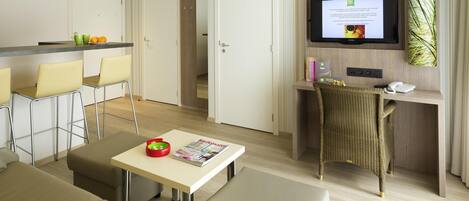 A modern hotel room with a dining area, a TV, and a seating area.