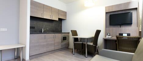 A modern, compact living space with a kitchenette, a flat-screen TV, a dining area, and a sofa.