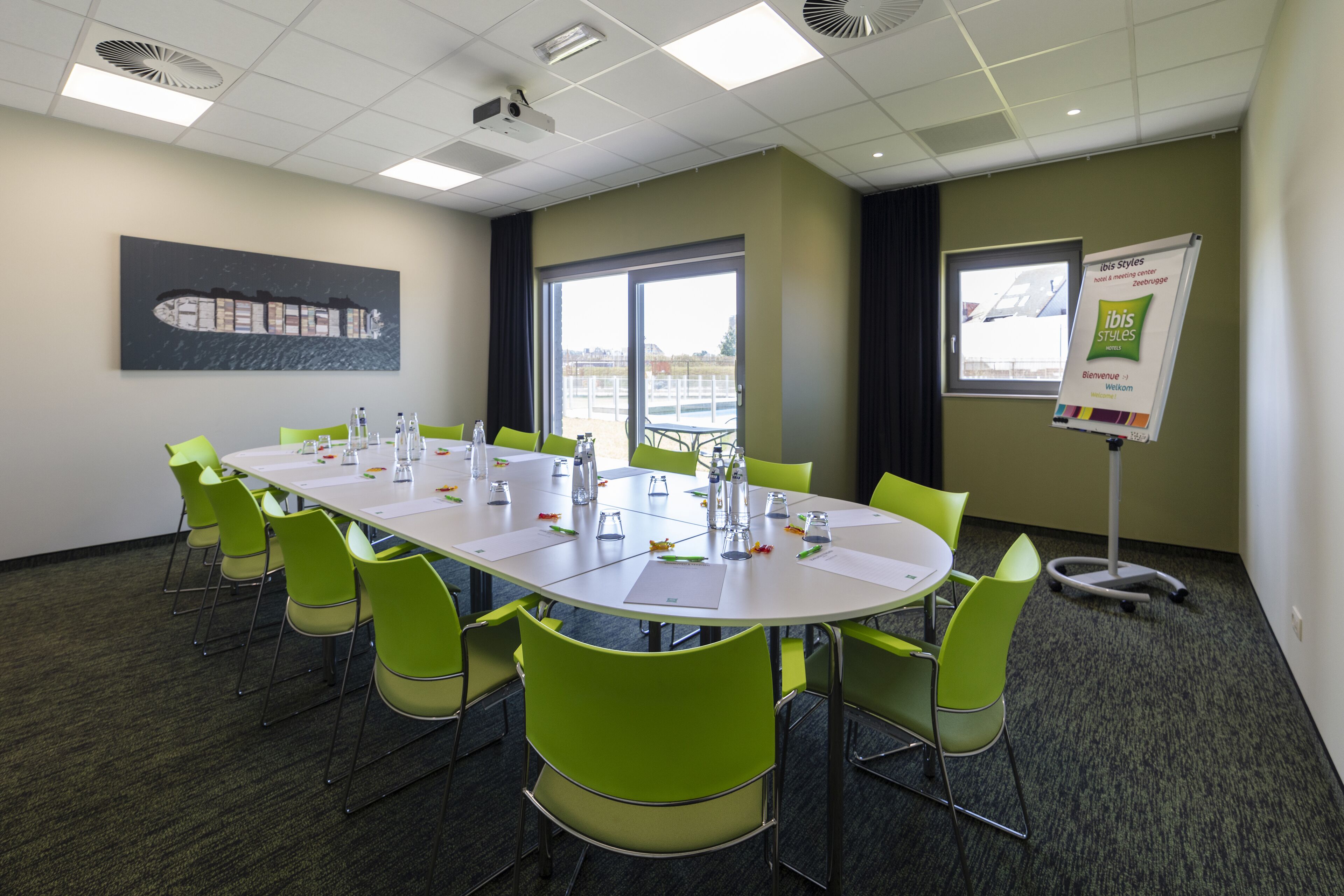 A conference room with a long table, green chairs, a projector, and a banner on the wall.