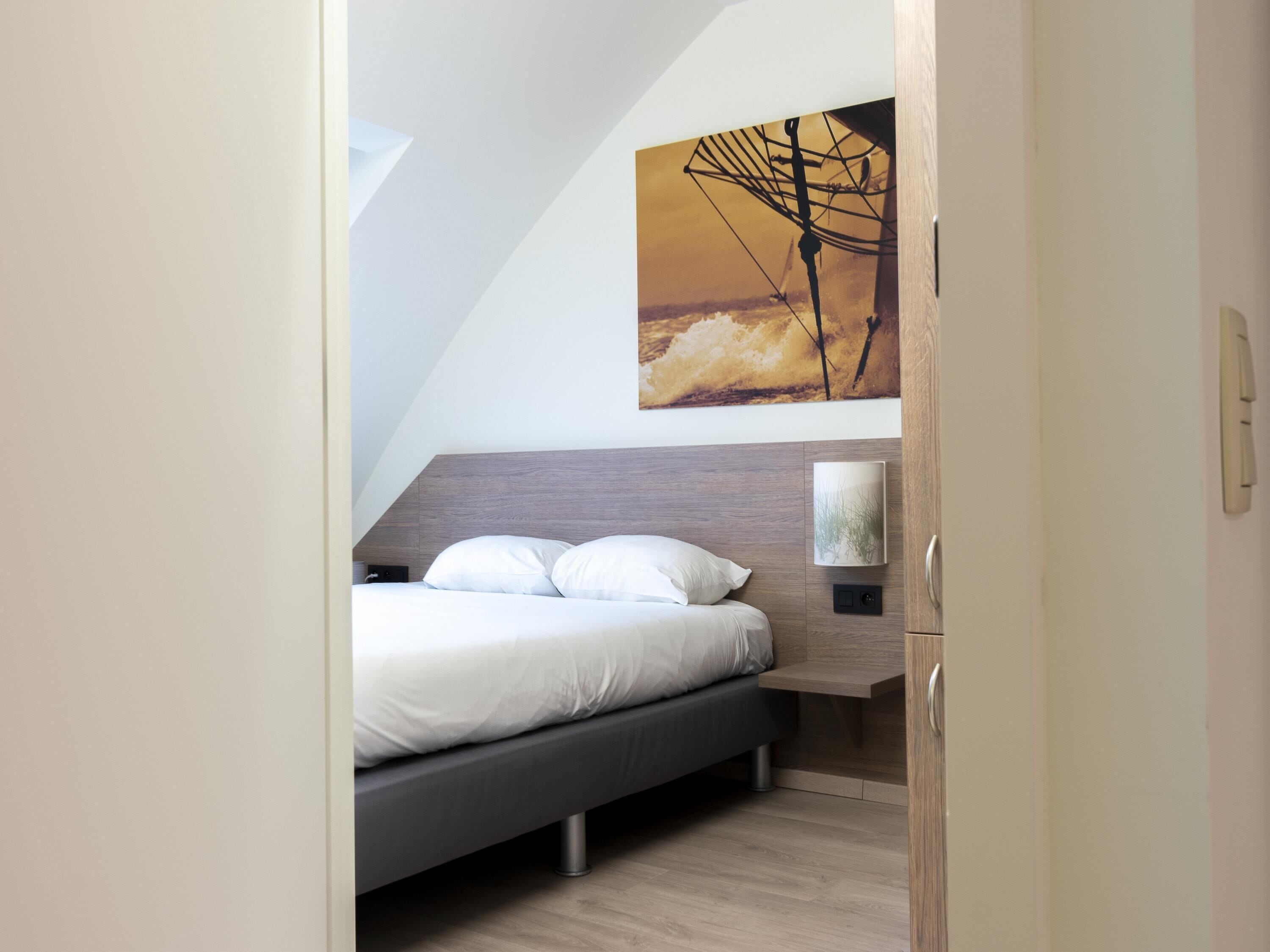 A bedroom with a bed, a nightstand, a wall-mounted lamp, and a painting.