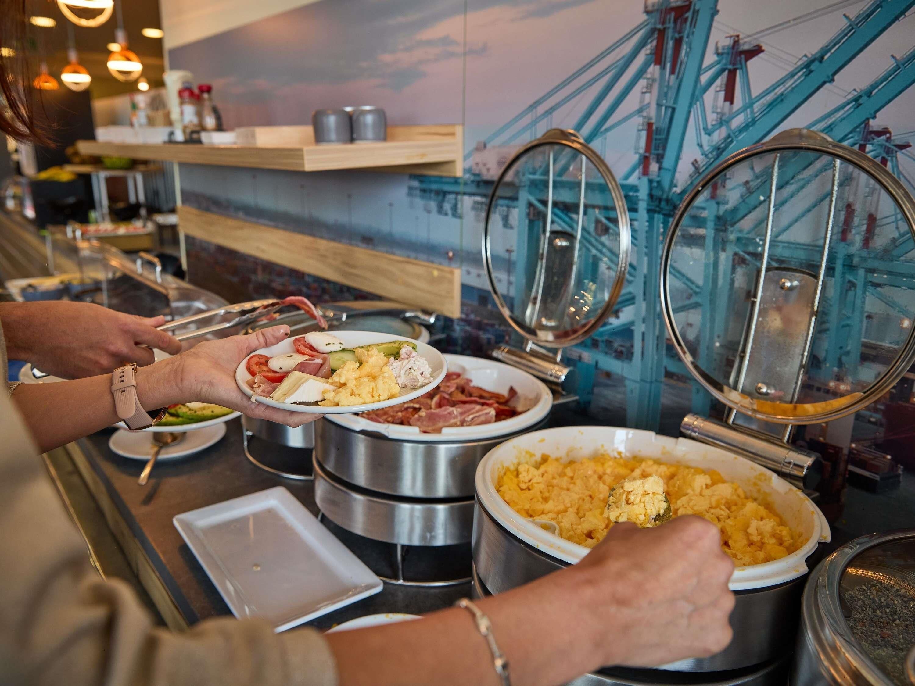 A buffet setup with various food items, including scrambled eggs, bacon, and a pot of mashed potatoes.