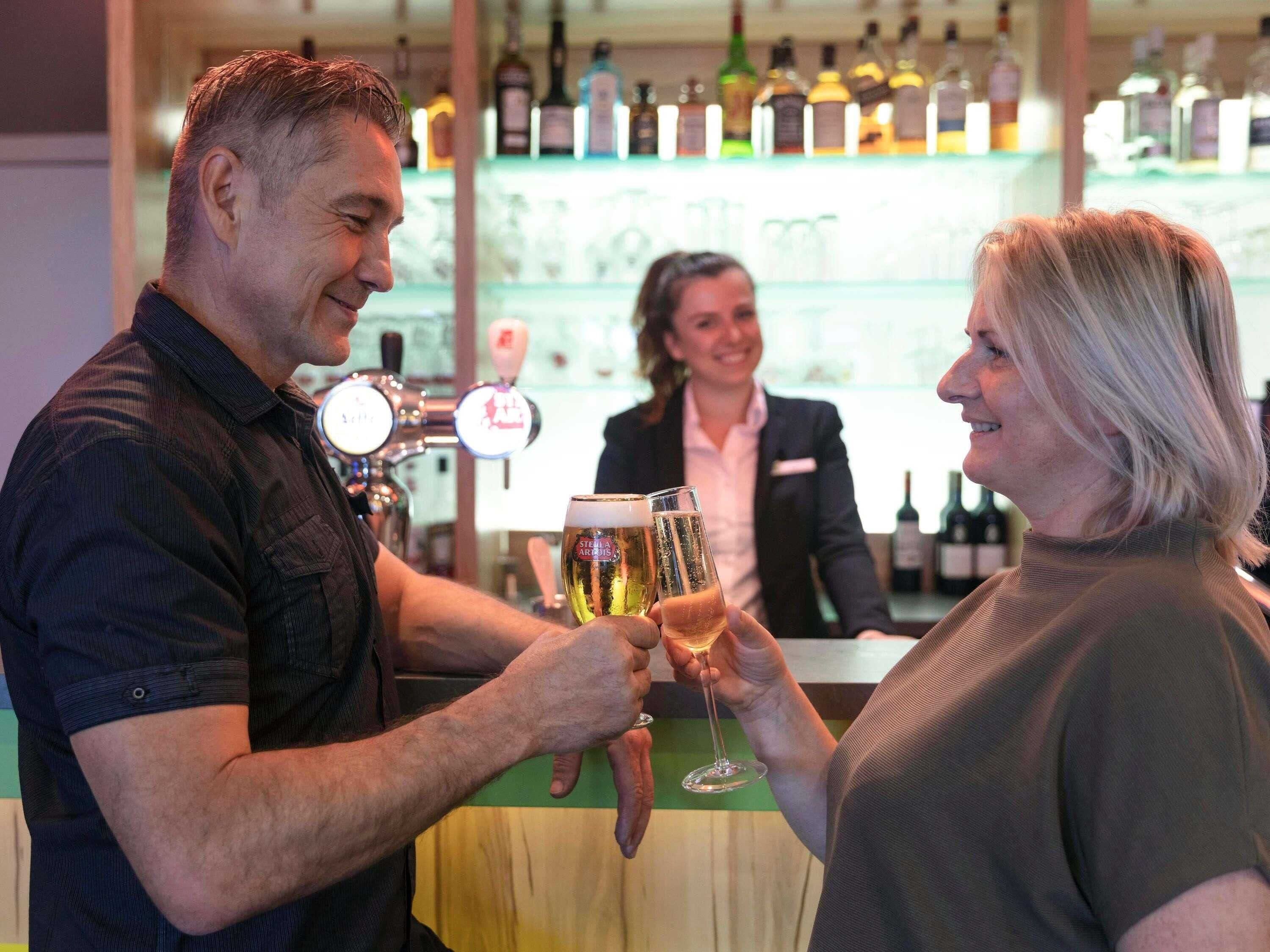 Eine Bar mit einem Barkeeper und zwei Gästen, die mit Gläsern anstoßen.