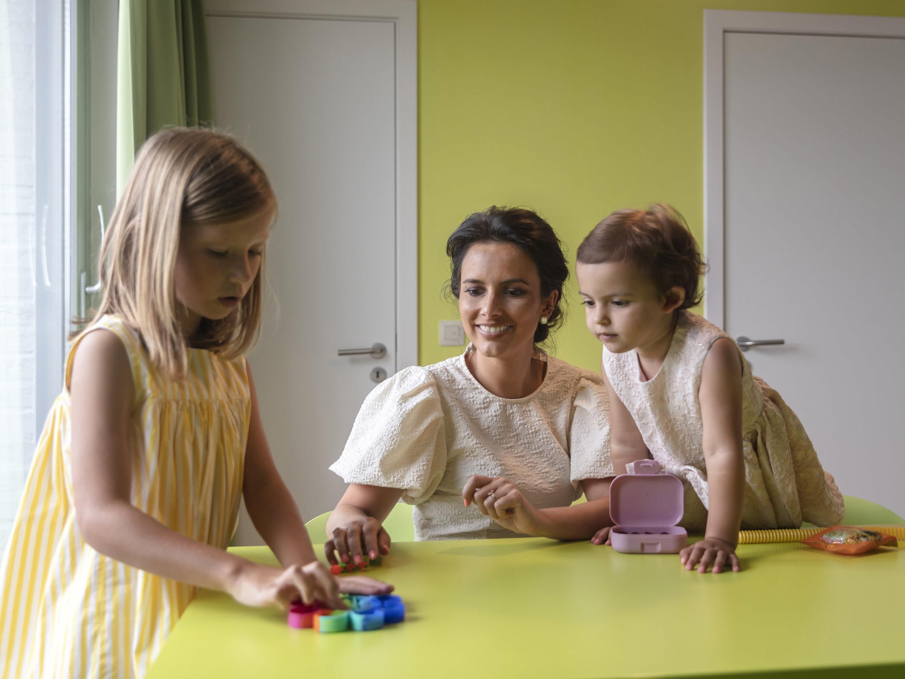 A room with a green table where three people are playing with colorful blocks.