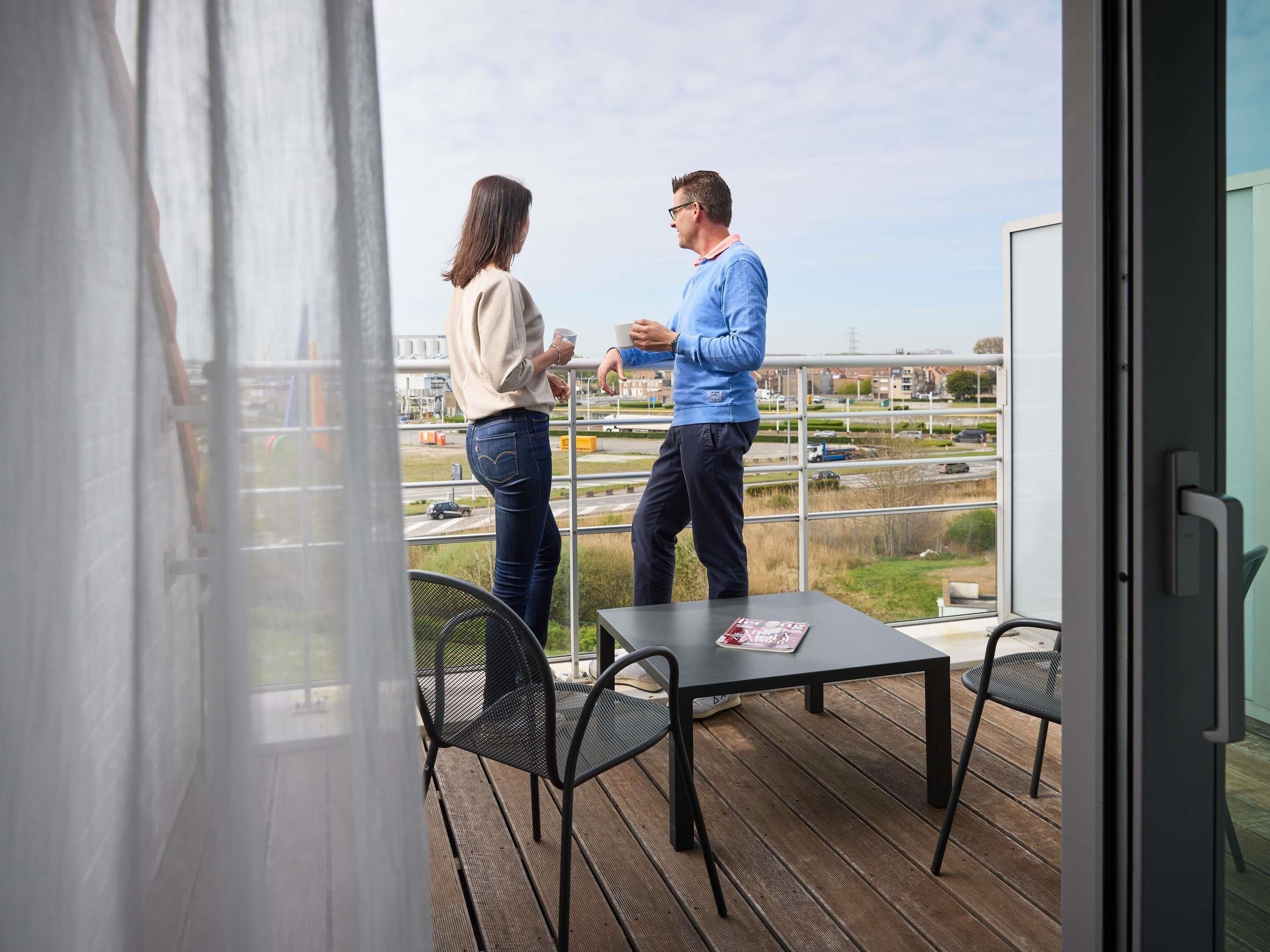 Un balcón con mesa y sillas, vista a la ciudad y un edificio con puerta de cristal.