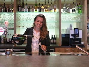 A bar area with a bartender pouring a drink, shelves with bottles, and glasses.