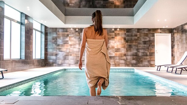 A person walking towards a pool in a modern indoor setting with stone walls and large windows. - ibis Styles Zeebrugge (Bruges)