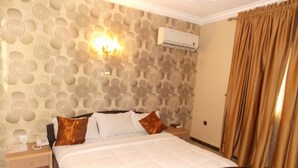 Una cama bien hecha con almohadas blancas y marrones, un cabecero de madera y un aire acondicionado instalado en la pared.