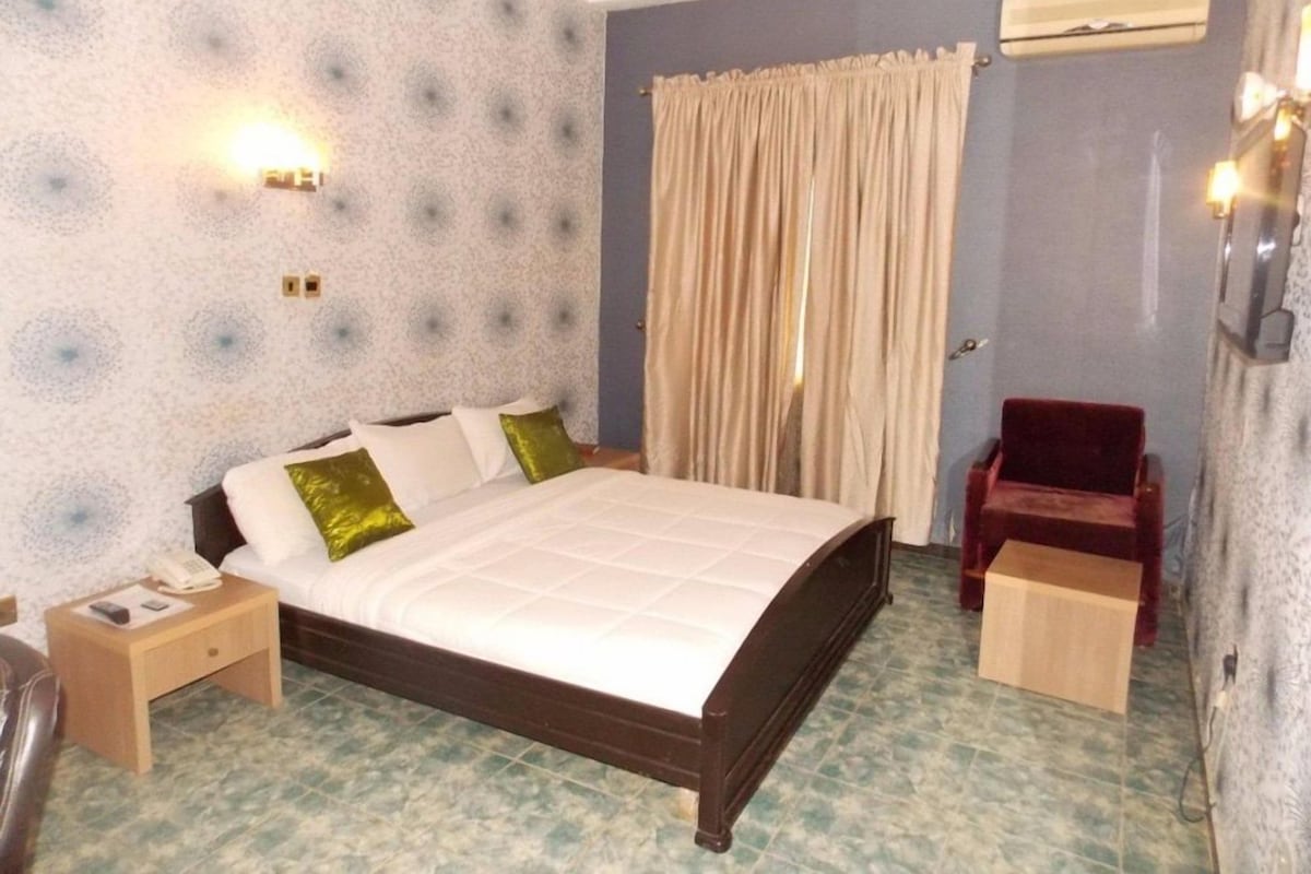Una camera d'albergo con un letto, un comodino e una sedia rossa.